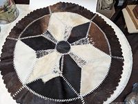 Top view of round cowhide patchwork mat showing geometric design and scalloped edge