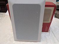 Front view of one speaker with grille in place, box behind