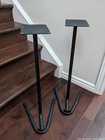 Two identical black steel speaker stands beside staircase