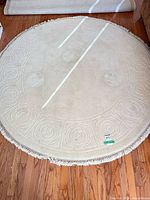 Full view of round cream rug showing embossed border and fringe