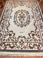 Full view of ivory floral medallion area rug with fringe