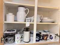 Cabinet shelves showing all ceramic pieces, mugs, and coffee grinder