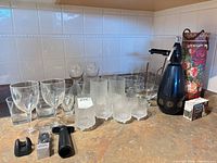 Overall lot showing wine glasses, coupes, textured tumblers, soda siphon, chargers, wine pump, bottle tote