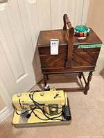 Brother yellow sewing machine on floor beside wooden cantilever box with pincushion on lid