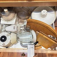 Drawer view showing blender base, food processor parts, hand mixer, cutting boards