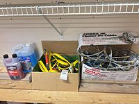 Full lot showing cable chain box, jumper cables, washer fluid jug and red fluid bottle on shelf