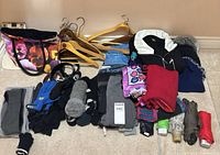 Lot overview showing clothing pile, hangers, tote, belts, gloves, scarves, umbrellas