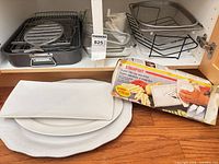 Overview of cabinet contents including roasting pan, glass dishes, mesh strainer on stand, white platters and boxed slicer