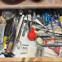 Drawer view showing majority of utensils including flatware, shears, red silicone bulb, corkscrew, graters