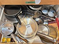 Drawer view showing mixed stainless pots, nonstick pans, lids, steamer, egg poacher cups and ramekins