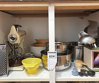 Cabinet shelf showing entire assortment including mixer, bowls, grater, utensils, measuring spoons and crock