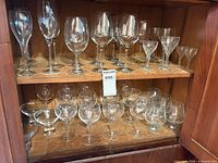 Two cabinet shelves filled with assorted clear stemmed wine and bar glasses of varying shapes and sizes