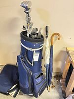 Full view of navy blue golf bag on pull cart with clubs and umbrella