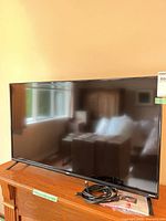 Front view of 42-inch TV on stand with power cable and remote visible