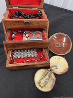Accordion jewelry box open showing drawers and jewelry pieces inside plus shell cases with rings and beaded necklace
