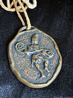 Front view of bronze amulet on twine cord showing relief warrior