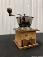 Front view of coffee grinder showing brand name, burlap panels, drawer, and metal bowl