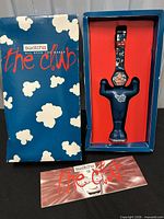 Outer box with clouds graphic and The Club logo beside figure stand holding watch