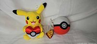 Front view of Pikachu plush with heart and Poké Ball plush