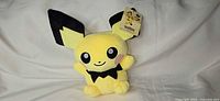 Front view of Pichu plush showing face, ears, bow-like neck marking, hang tag visible