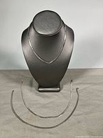 All three silver choker necklaces displayed on stand and surface