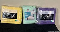 Three sealed sheet sets in yellow, mint green floral, and purple packaging
