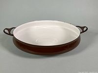 Side view of brown Dansk Kobenstyle paella pan showing white interior and handles