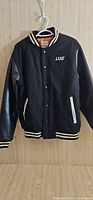 Front of black Lug varsity jacket hanging on hanger