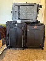 Front view of three wheeled suitcases: two black large spinners side by side, grey medium spinner stacked on top