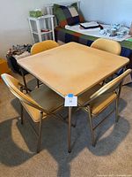 Square beige folding card table with four matching chairs around it