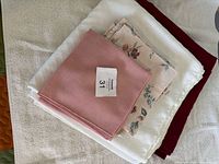 Stack of folded linens: white tablecloths, burgundy cloth, dusty pink napkins, floral napkins