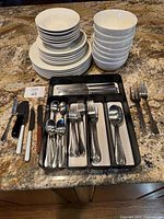 Stacks of white dinnerware and assorted flatware displayed on countertop