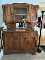 Front view of carved wood mirrored breakfront showing upper glass cabinet, marble top, drawers, and lower cupboards