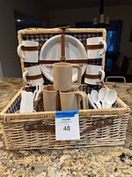 Open wicker picnic basket showing contents including plate, cups, mugs and flatware