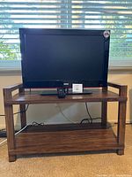Front view of RCA TV on two-shelf wooden stand with remote control on top shelf
