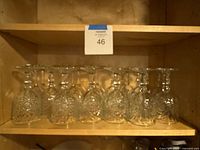Row of ten matching cut glass goblets inverted on wooden shelf
