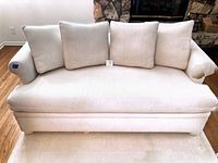 Front view of cream white sofa showing bench cushion, four pillows, and wear on arms