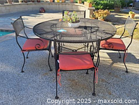 Full view of round wrought iron patio table and four matching chairs with red cushions set on outdoor surface