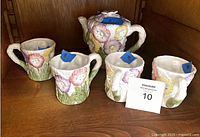 Front view of ceramic pansy teapot with lid and four matching mugs on shelf