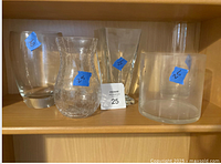 Shelf view of five clear glass vases showing shapes and sizes