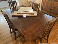 Dining table with leaves and pads stacked on top, chairs arranged around