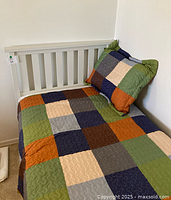 White twin headboard with patchwork comforter and sham on frame