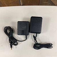 Front view of two SEGA MK-2103 adapters with cords and barrel plugs