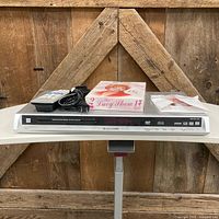 Front view of Panasonic DVD player with cord, remote, DVD box set, loose disc visible