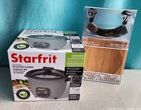 Boxed Starfrit 10-cup rice cooker and boxed mezzaluna mincing set side by side