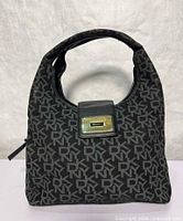 Front view showing monogram canvas, leather flap with DKNY gold-tone plaque, handle shape