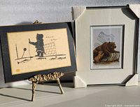 Both signed prints side by side; Inuit fishing scene on easel, bear print matted with corner protectors