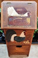 Front view showing entire wooden bin with painted hen on lid and rooster on body