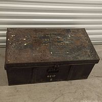 Full view of closed metal chest showing lid lettering and latch