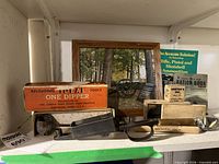 Overall lot on shelf showing dipper box, booklets, wooden block, framed photo and cartridges